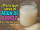 Vaso de vidrio con agua de arroz fermentada sobre mesa de madera y arroz crudo, con texto: “¿Para qué sirve el agua de arroz fermentada?”