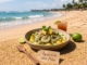 Ceviche de camarón y piña fresco en cuenco rústico sobre arena de playa. Tenedor de madera y cóctel de fondo.